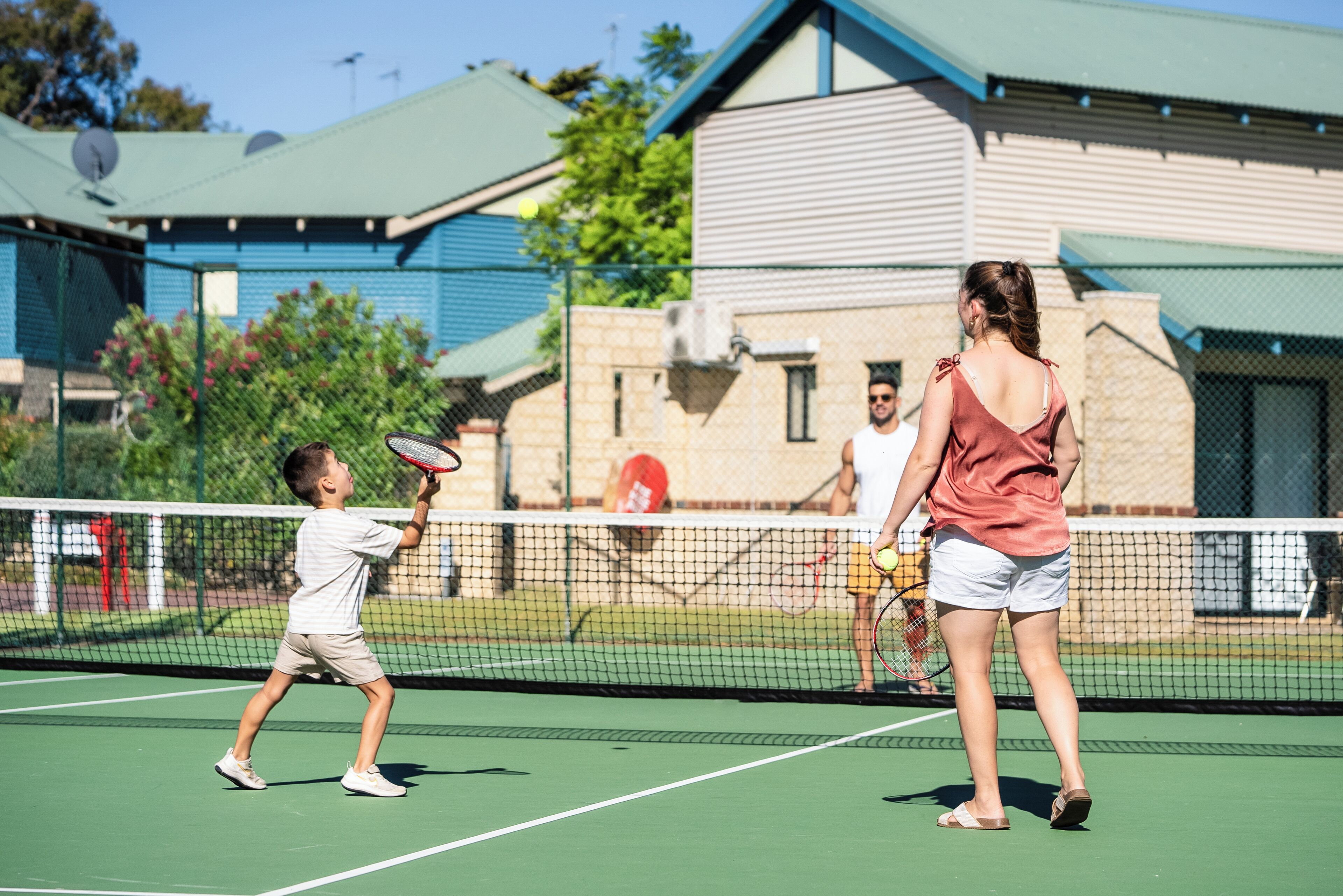 A tennis court with a net, a player in a white shirt, and a coach in a pink top.