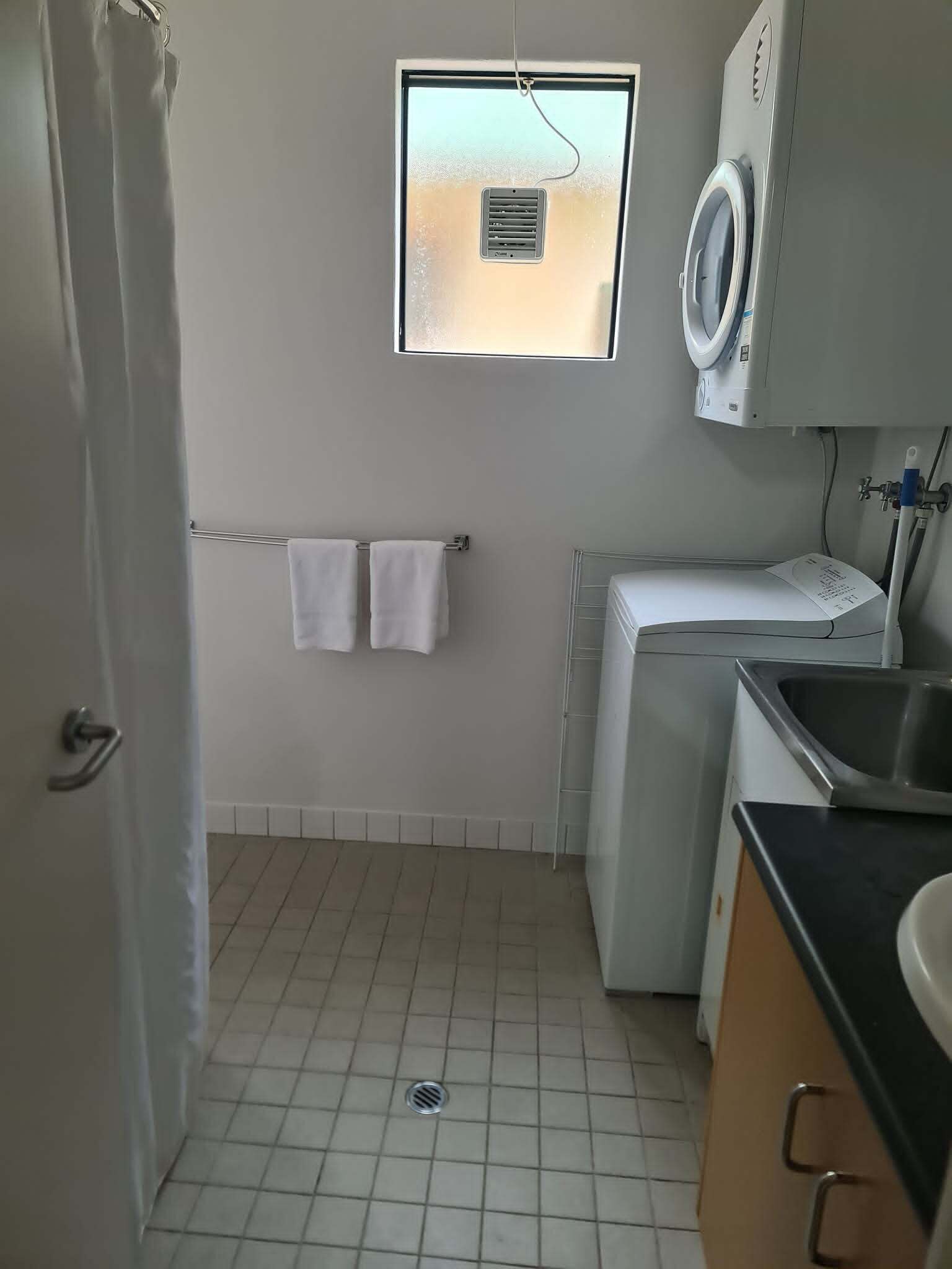 Een compacte, schone wasruimte met een wasmachine, een droogrek en een raam.