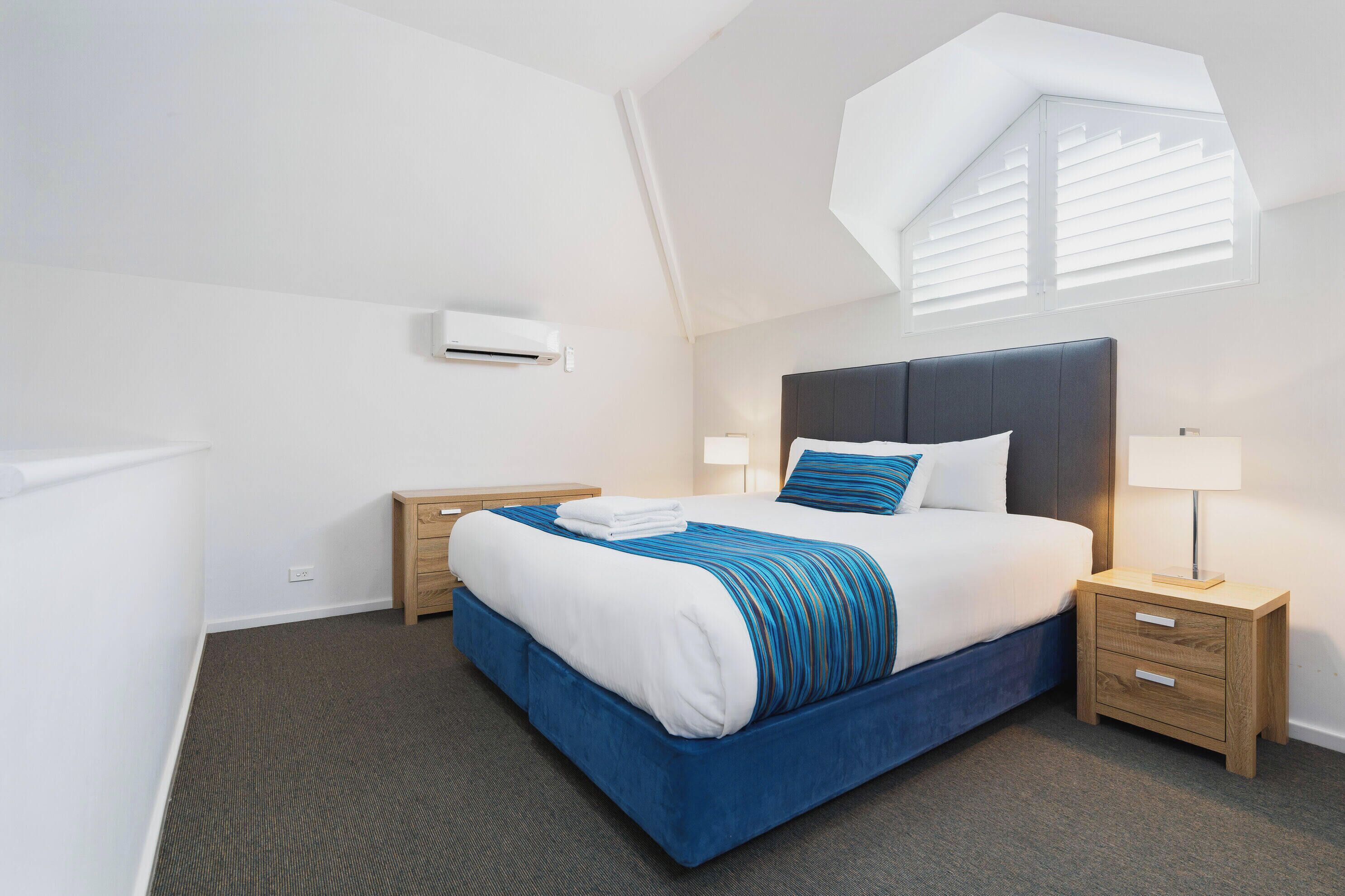 A modern hotel room with a large bed, a wooden nightstand, a desk, and a skylight.