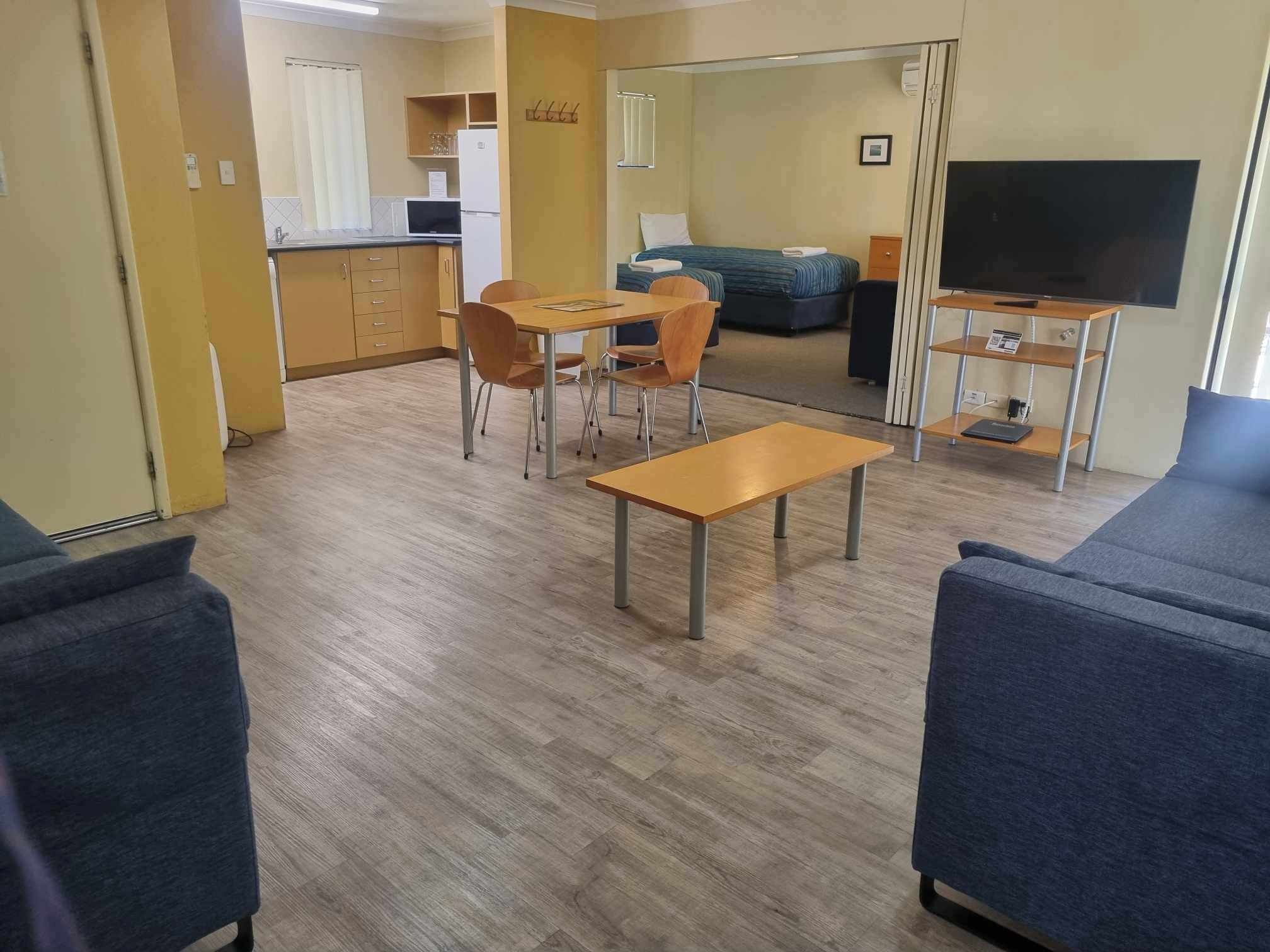 Una habitación de hotel con kitchenette, comedor con mesa y sillas, sofá, televisión y cama.