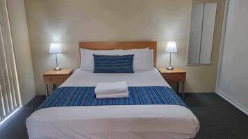 Une chambre d’hôtel avec un grand lit, deux tables de chevet avec des lampes, un miroir et une fenêtre avec des stores.