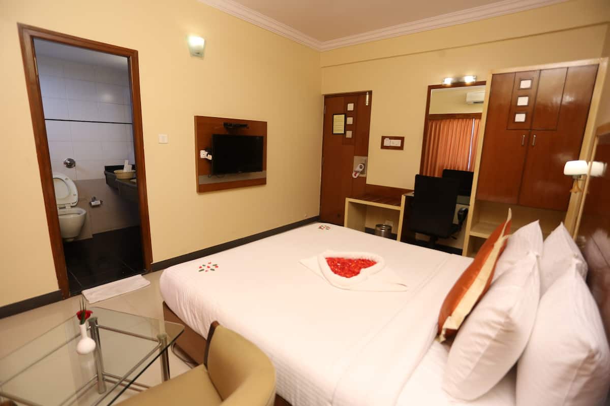 A hotel room with a bed, a TV, a desk, and a bathroom visible through an open door.