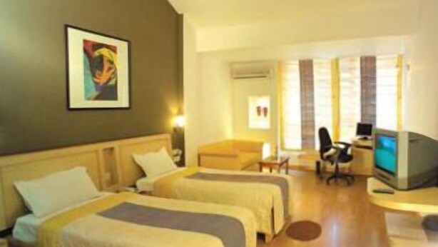 A hotel room with two beds, a desk with a computer, a TV, and a painting on the wall. - Hotel Nandhini Whitefield (Bengaluru)