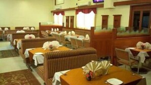 A hotel dining area with booths and tables, air conditioning units, and a television on the wall. - Hotel Nandhini Whitefield (Bengaluru)