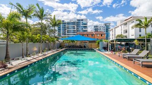 A swimming pool with lounge chairs and umbrellas, surrounded by palm trees and modern buildings in the background. - Broadwater Keys (Labrador)