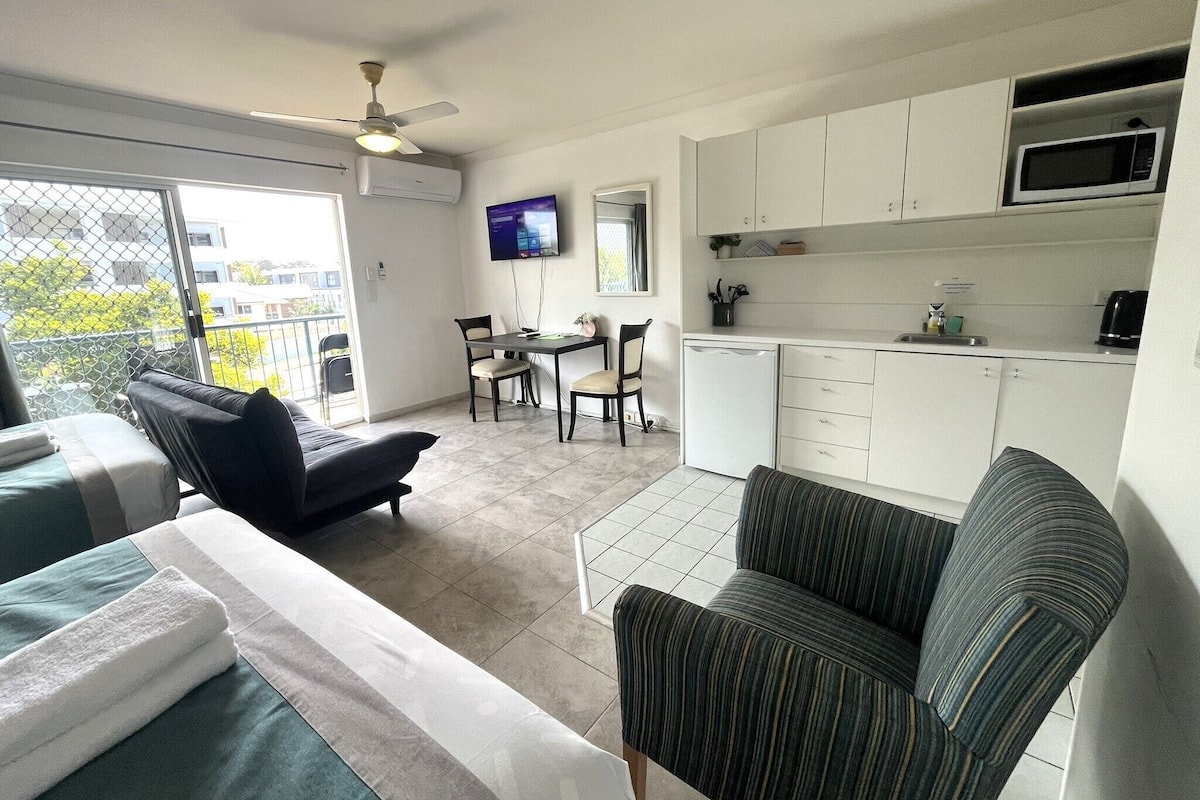 A compact living space with a kitchenette, a dining area, and a balcony with a view.