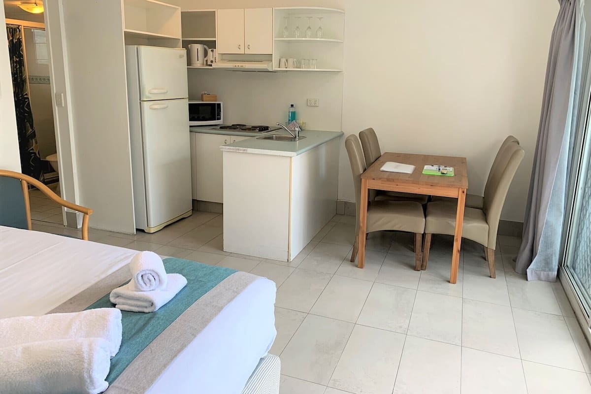 A compact hotel room with a bed, a small kitchenette, a dining table with chairs, and a view of the outside.