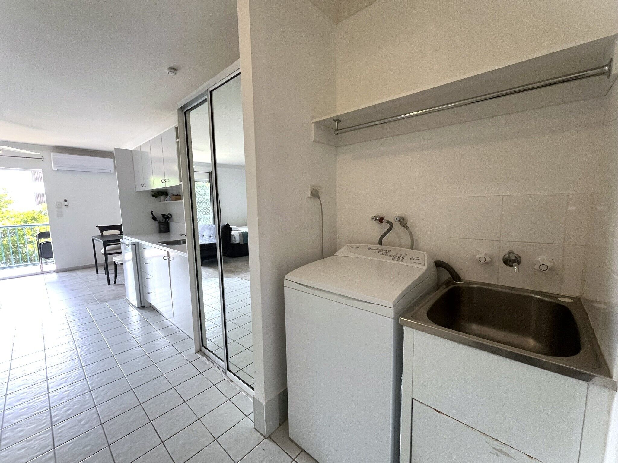 A modern kitchen with a built-in washing machine, a stainless steel sink, and a glass door leading to a balcony.