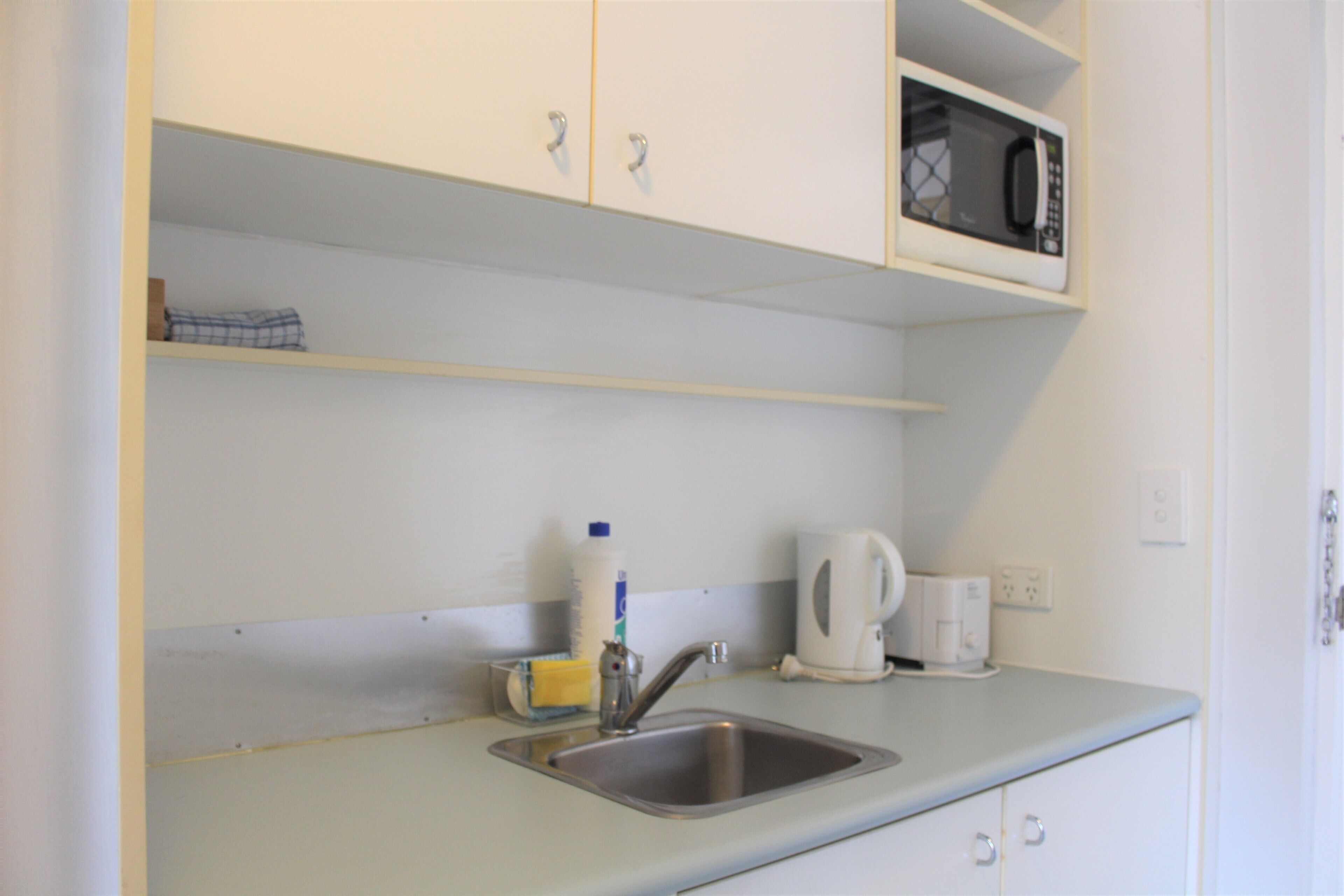 Una cocina con un fregadero, un microondas, un hervidor y una botella de detergente.