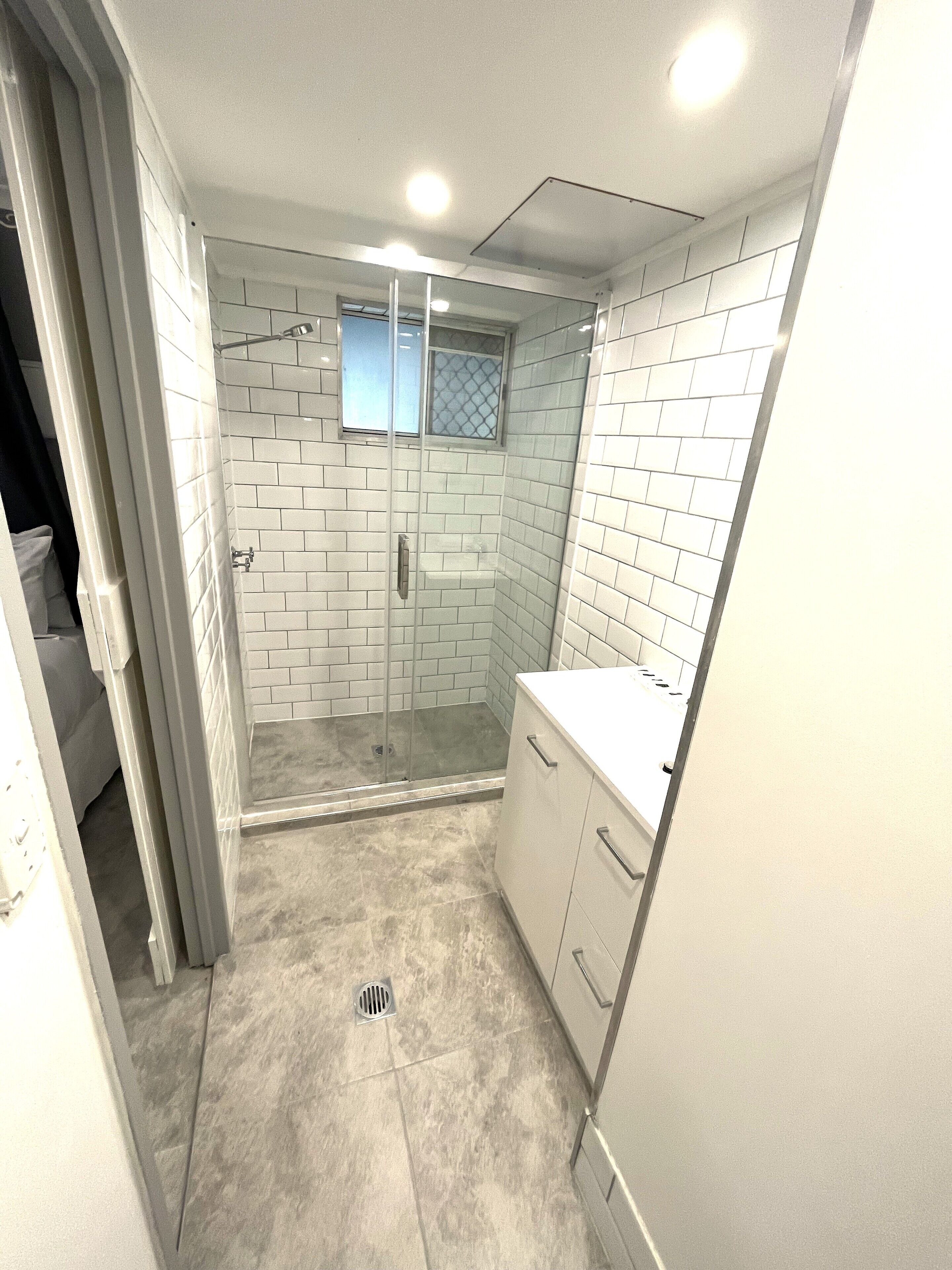 Une petite salle de bain moderne avec des carreaux de céramique blancs rectangulaires, une douche en verre et un comptoir blanc.