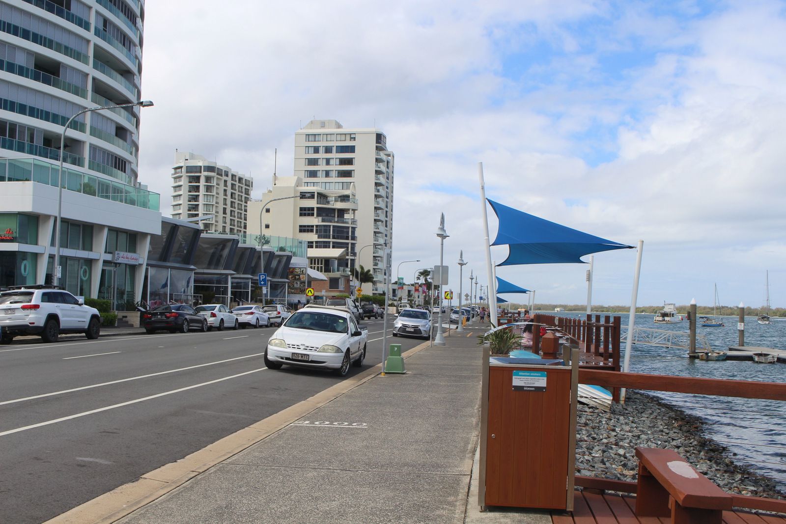 Una calle junto al agua con edificios modernos, una acera para peatones y automóviles estacionados.