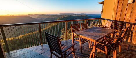 A wooden deck with a table and chairs, overlooking a mountainous landscape.