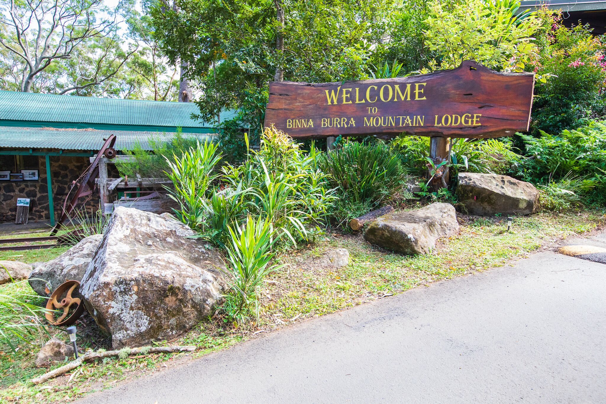 A wooden welcome sign for Binna Burra Mountain Lodge surrounded by rocks and greenery.