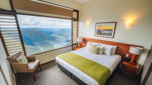 A hotel room with a large bed, a chair, a nightstand, and a view of a mountainous landscape through a large window. - Binna Burra Sky Lodges (Binna Burra)