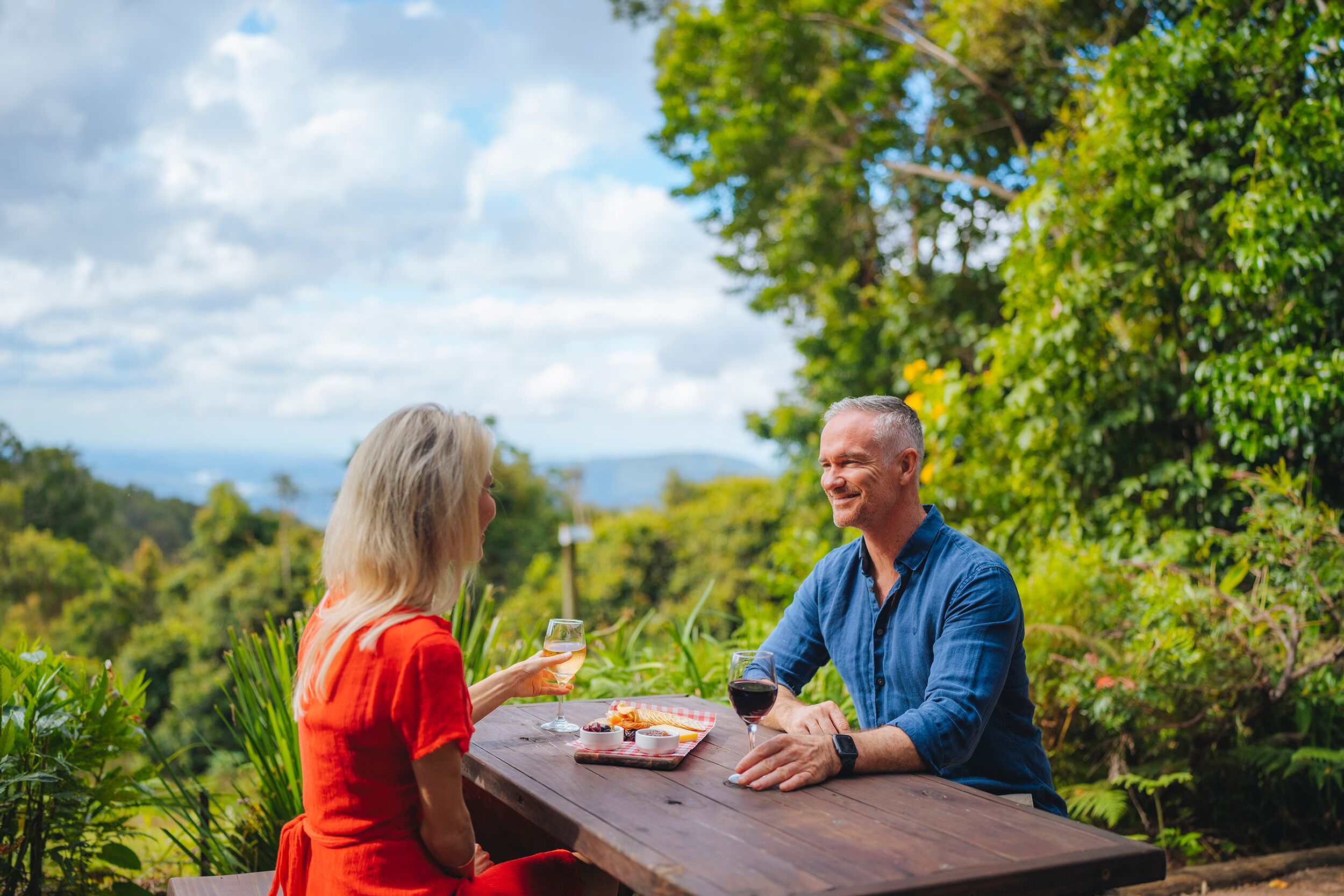 A couple dining at an outdoor table with a scenic view of greenery and mountains in the background.
