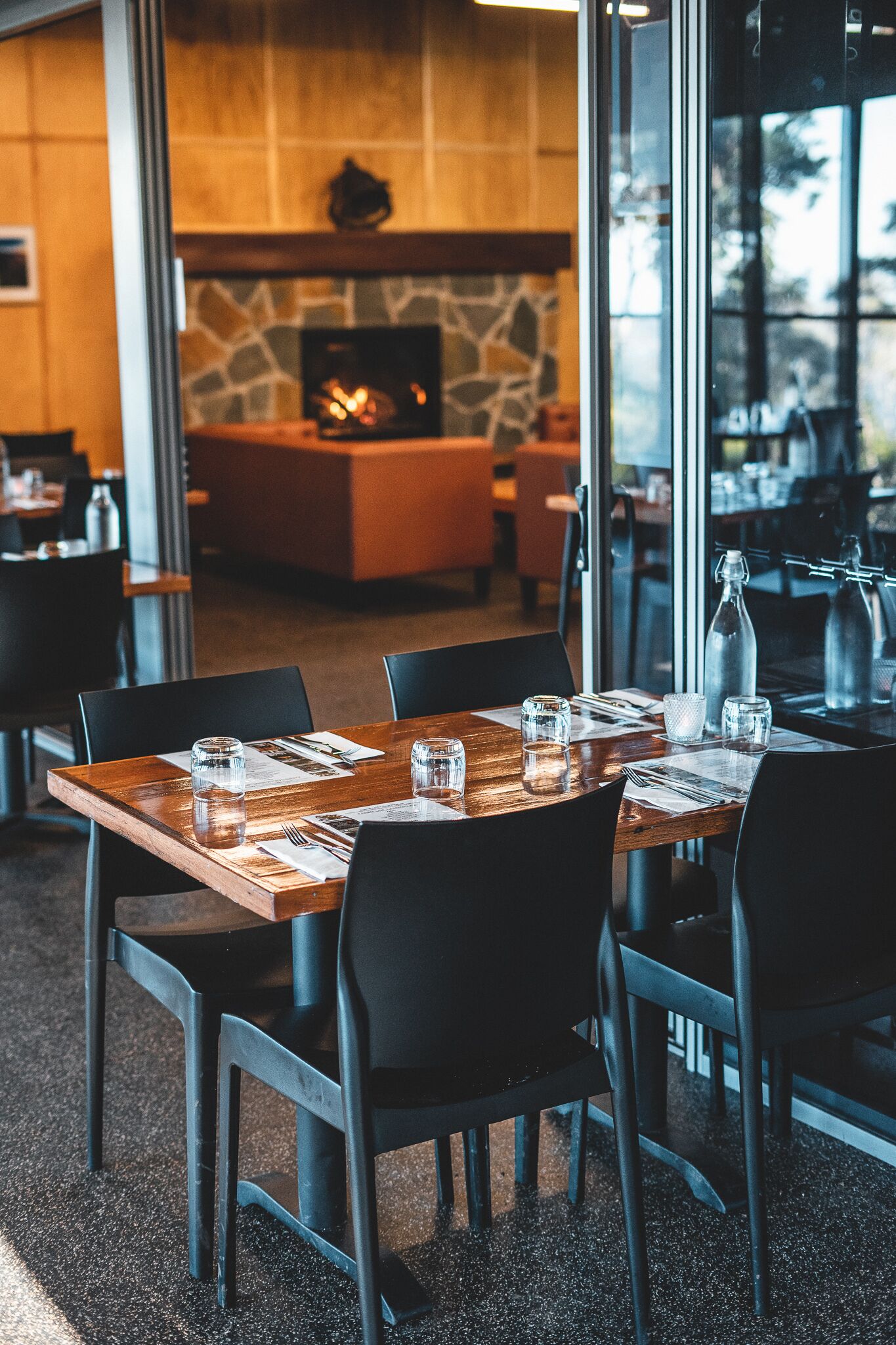 A restaurant with a stone fireplace, wooden tables, and black chairs.