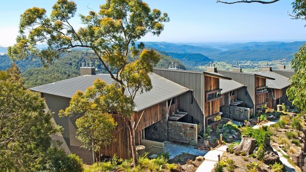 A modern multi-story building with a flat roof, surrounded by natural vegetation and a clear view of distant hills. - Binna Burra Sky Lodges (Binna Burra)