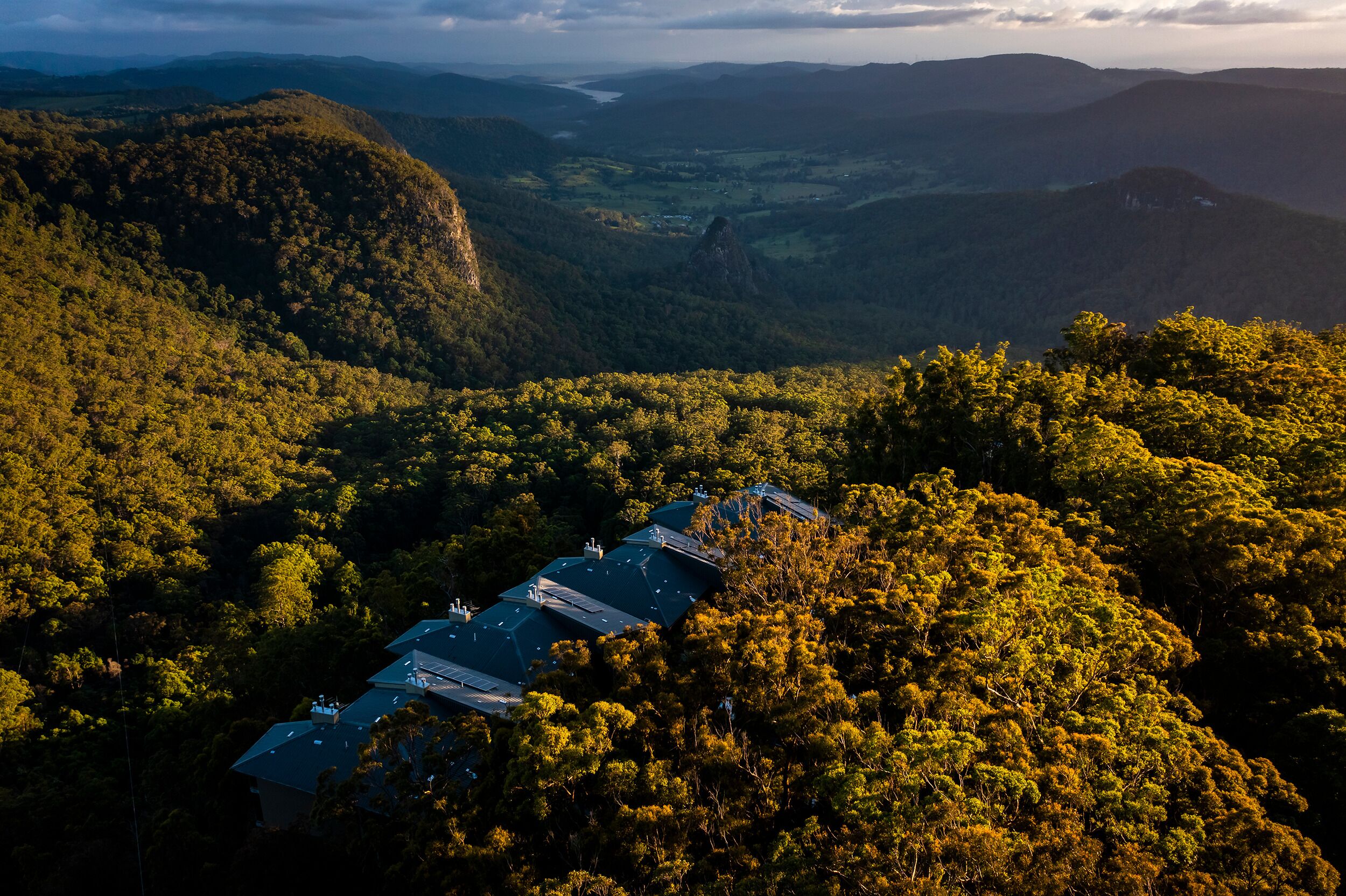 Una zona boscosa y aislada con un grupo de edificios, probablemente un albergue o resort, rodeado de árboles densos y colinas.