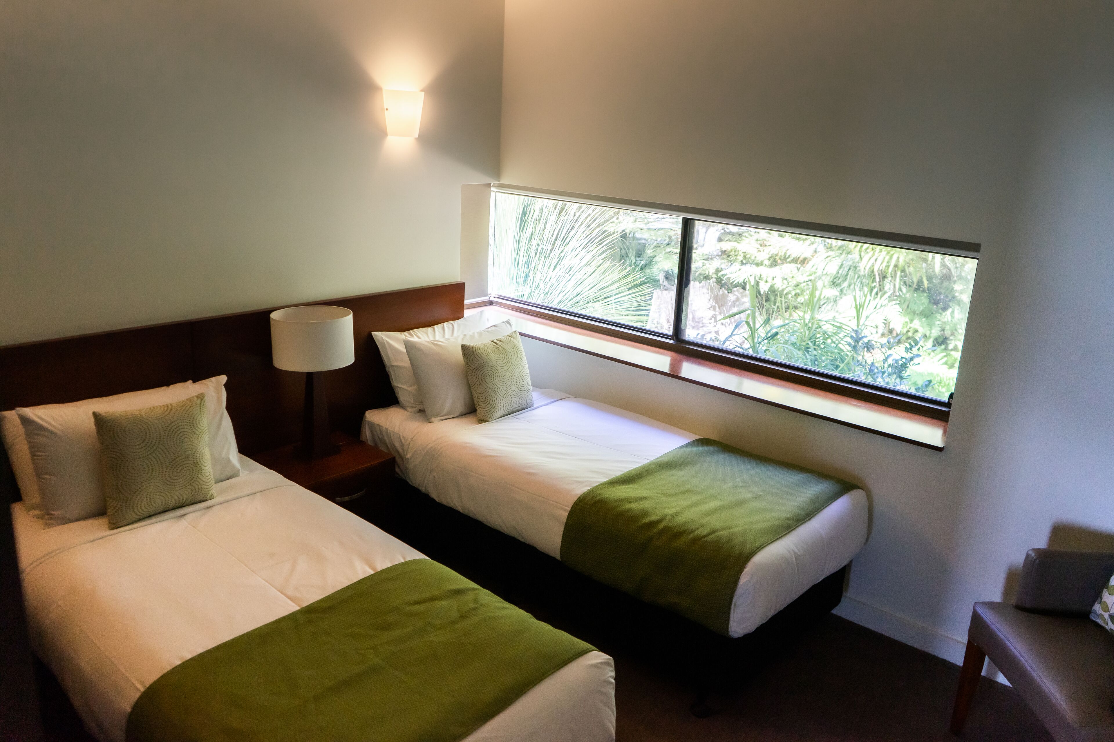 Une chambre d’hôtel avec deux lits, une table de chevet, une lampe et une fenêtre donnant sur un paysage verdoyant.