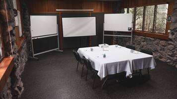 Un salón de conferencias con una mesa blanca, sillas y dos pizarras blancas.