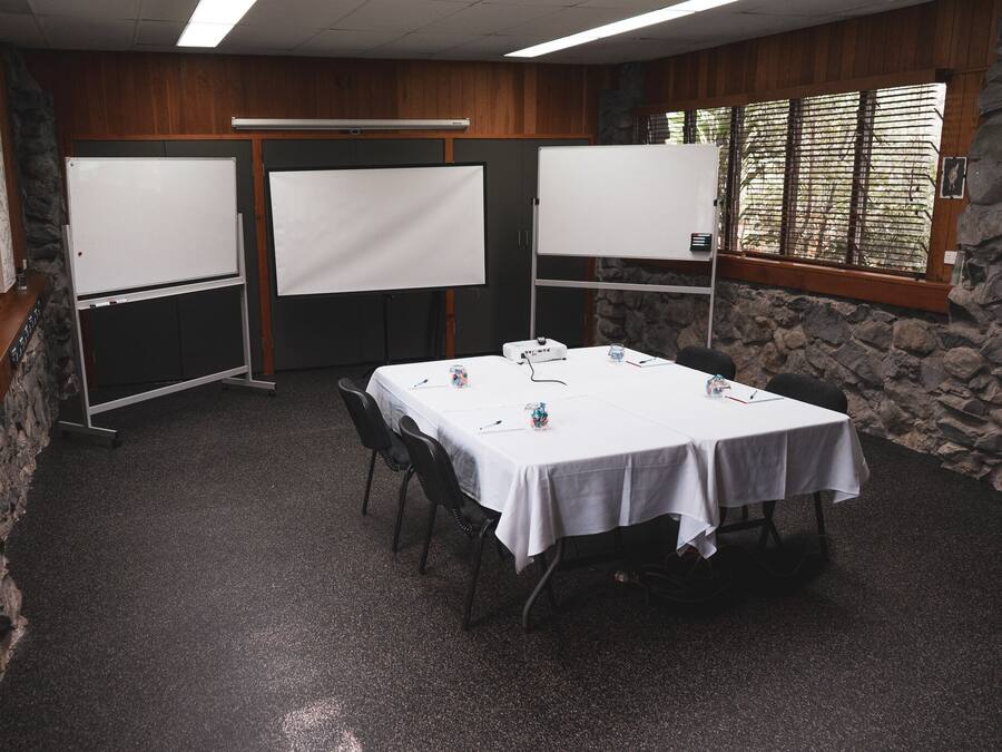 Un salón de conferencias con una mesa blanca, sillas y dos pizarras blancas.
