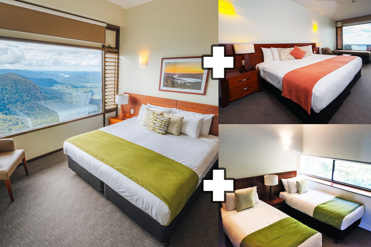 Habitación de hotel con un ventanal grande que ofrece vistas panorámicas, una cama con manta verde, una mesita de noche con lámpara y una silla con cojín.