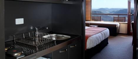 A compact kitchen with a stove, sink, and a small refrigerator. A balcony with a bed and a view of the mountains is visible.