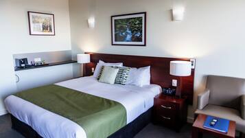 A neatly arranged hotel room with a large bed, bedside tables, a chair, and artwork on the walls.