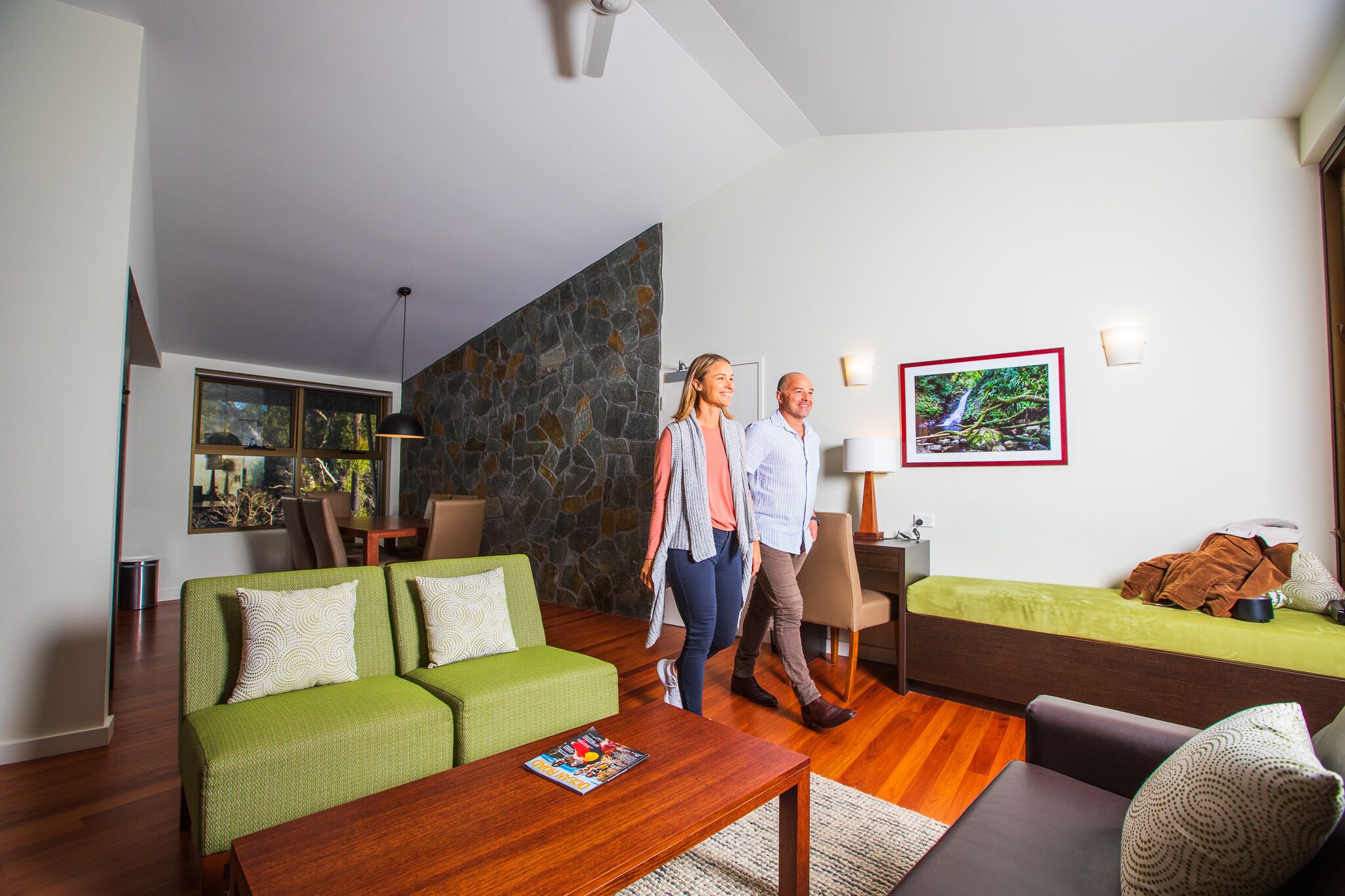 A modern living room with a green sofa, a wooden coffee table, and a stone accent wall.