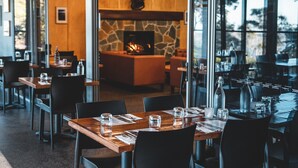A restaurant with a stone fireplace, wooden tables, and black chairs. - Binna Burra Sky Lodges (Binna Burra)