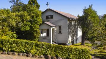 A small, single-story church with a cross on the roof, surrounded by well-maintained hedges and trees.