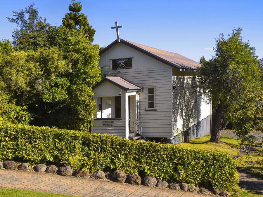 A small, single-story church with a cross on the roof, surrounded by well-maintained hedges and trees.