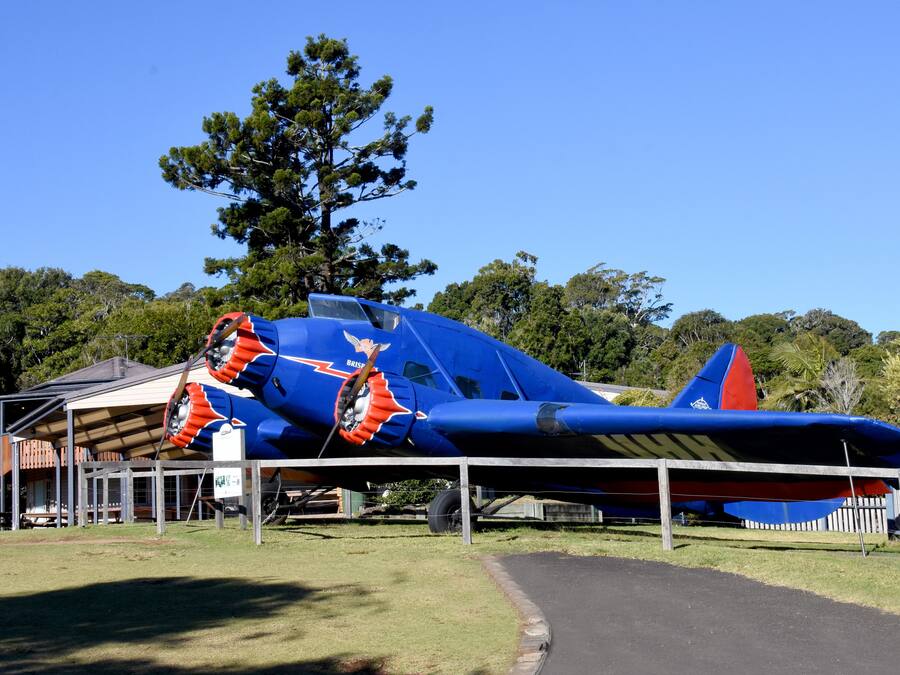 Um avião azul com detalhes vermelhos, estacionado sob um abrigo.