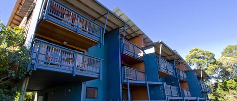 Un edificio de varios pisos con balcones, techo plano y un cielo azul despejado.
