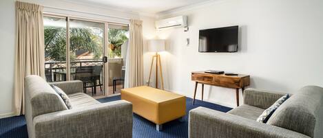 A modern hotel room with a sofa, ottoman, and a flat-screen TV.