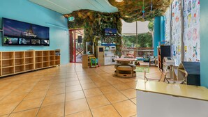 A spacious lobby with a large Disney-themed TV, a play area with a table and chairs, and a wall decorated with children's drawings. - Turtle Beach Resort (Mermaid Beach)