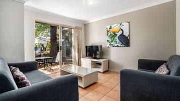A living room with grey sofas, a glass coffee table, a TV on a white stand, and a painting of a toucan on the wall.