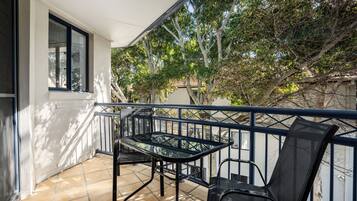 A balcony with a table and chairs, a railing, and a view of trees and buildings.