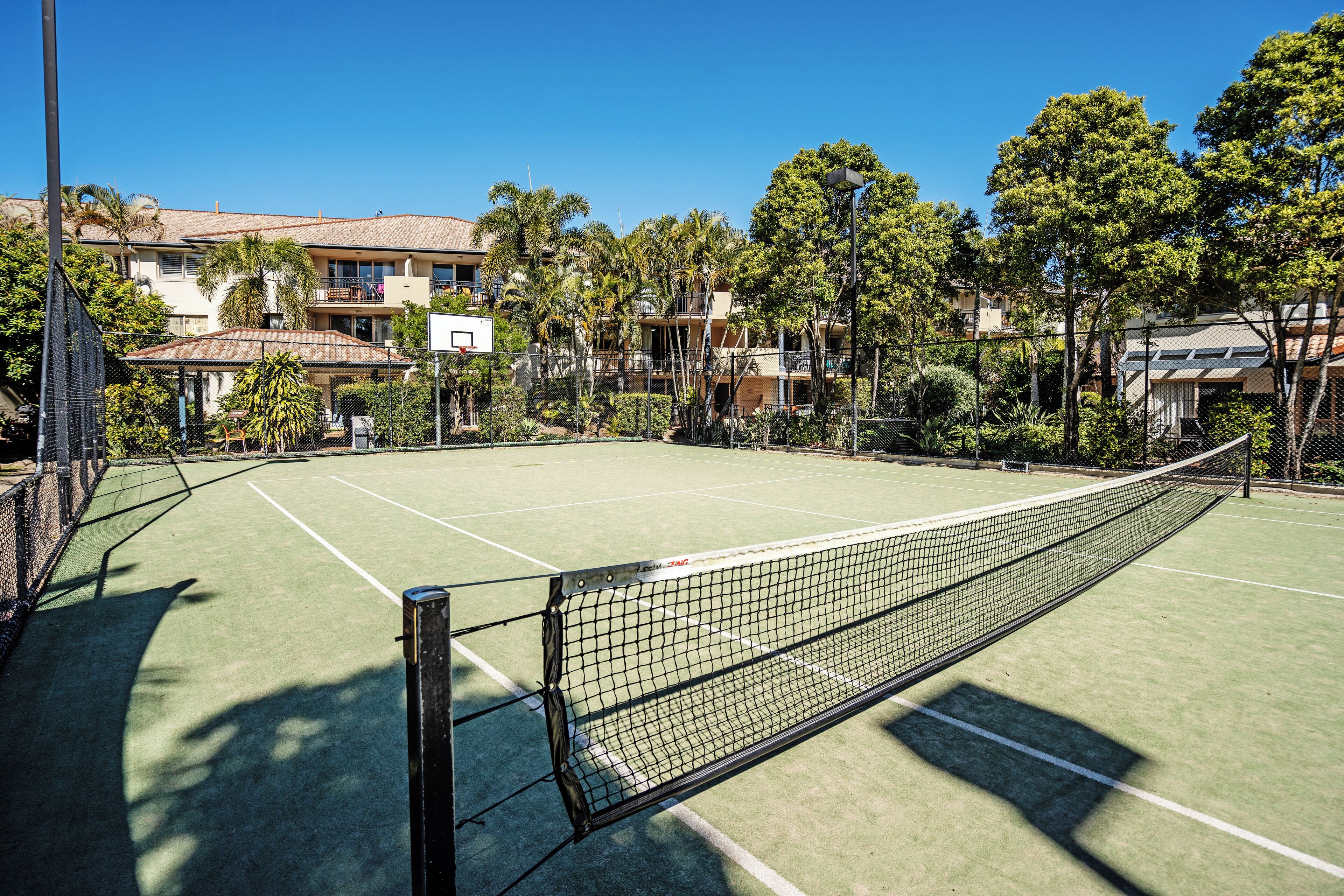 A tennis court with a net, surrounded by trees and buildings.
