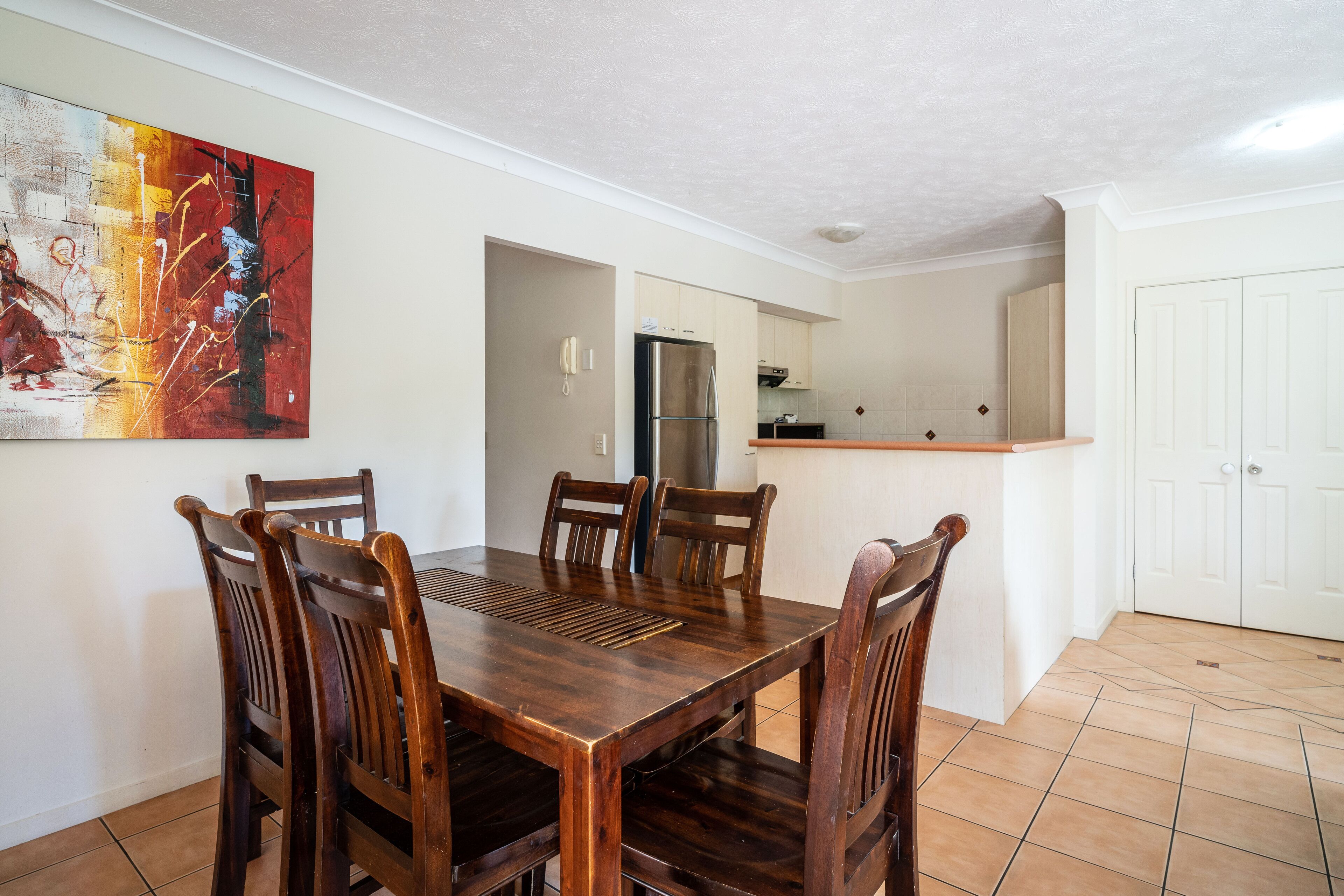 Un coin repas avec une table et des chaises en bois, une cuisine en arrière-plan et une porte blanche.