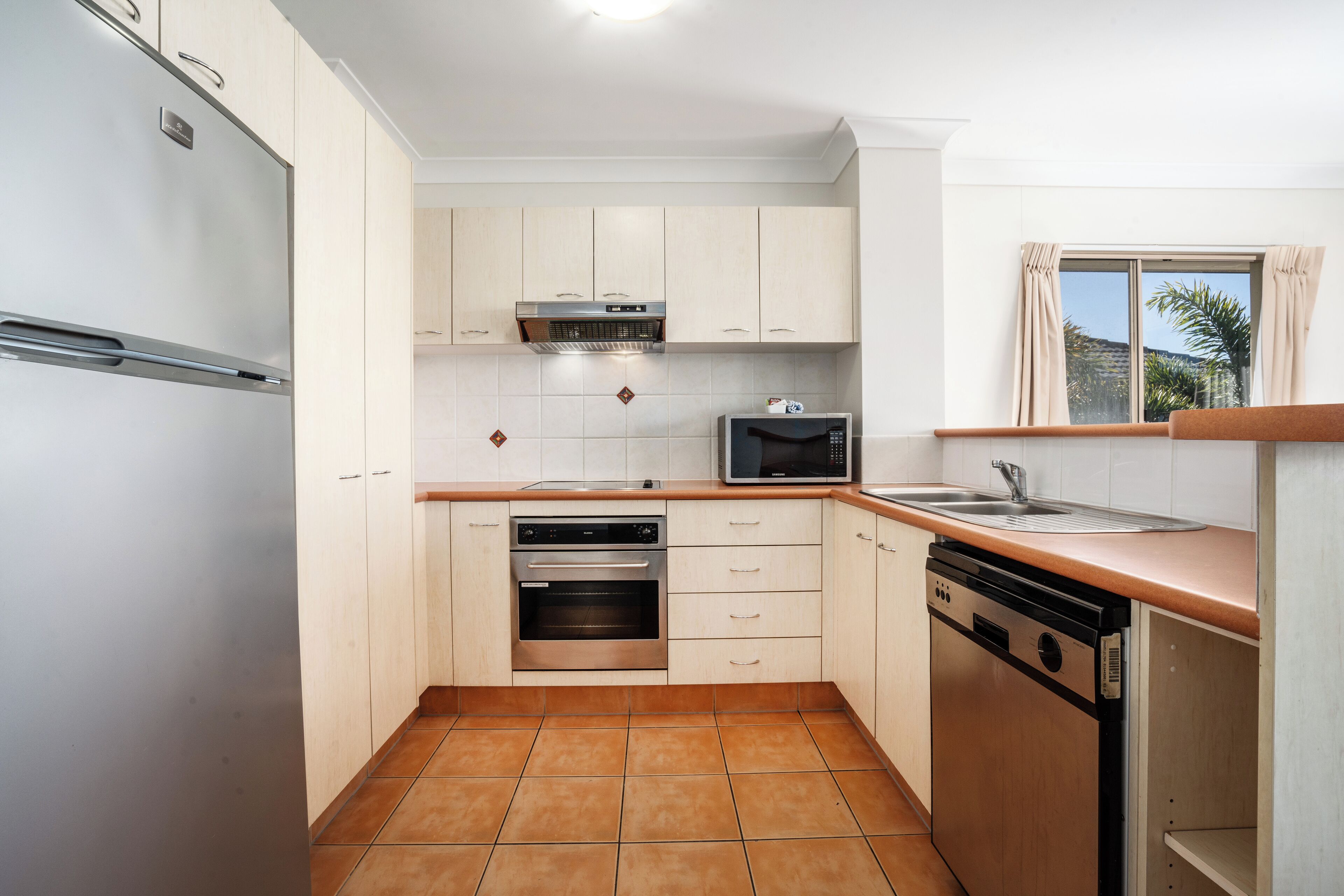 A modern kitchen with white cabinets, a stainless steel refrigerator, an oven, a microwave, and a dishwasher.