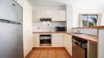 A modern kitchen with white cabinets, a stainless steel refrigerator, an oven, a microwave, and a dishwasher.