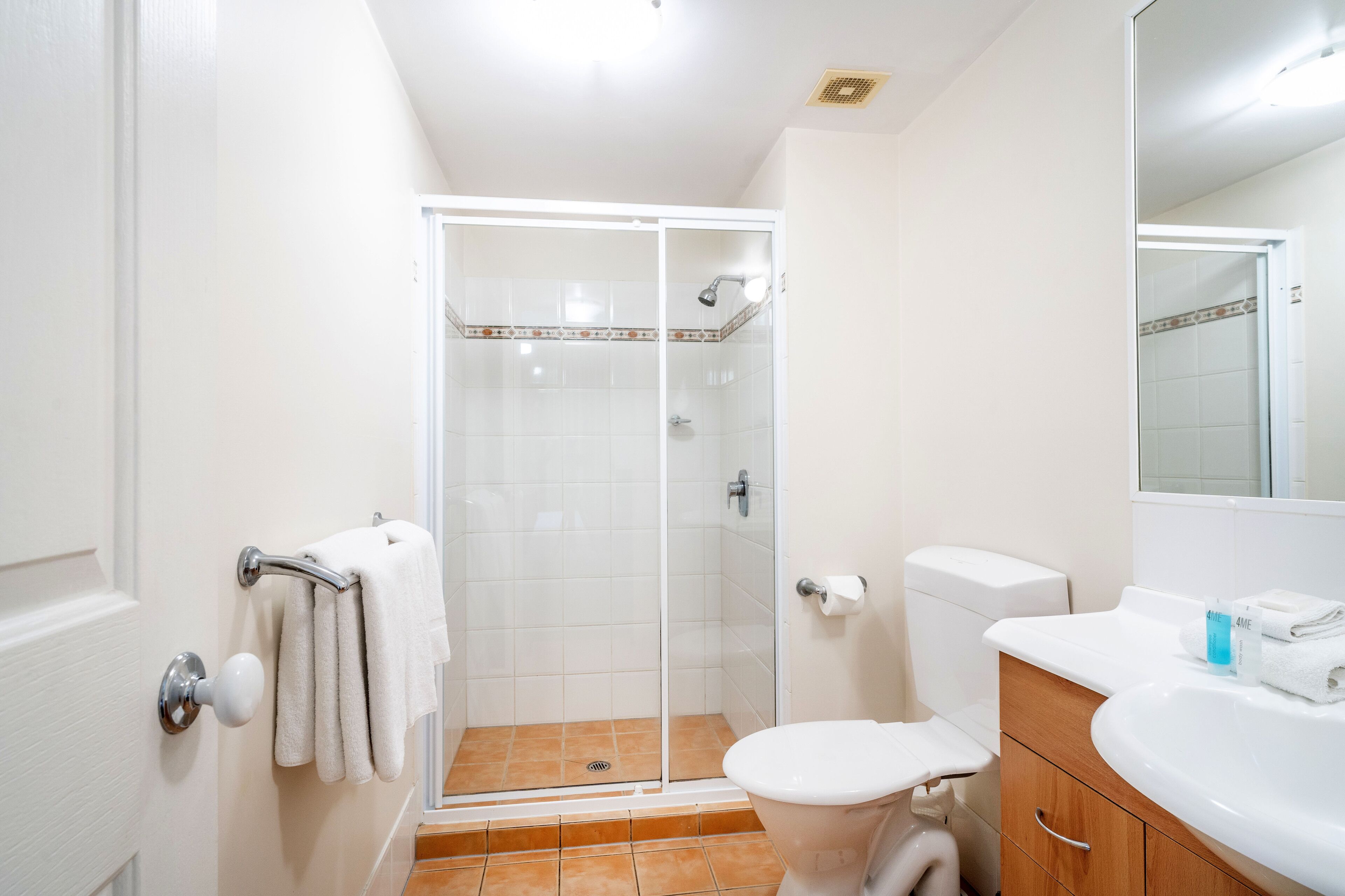 A bathroom with a glass-enclosed shower, a toilet, and a sink with a mirror above it.
