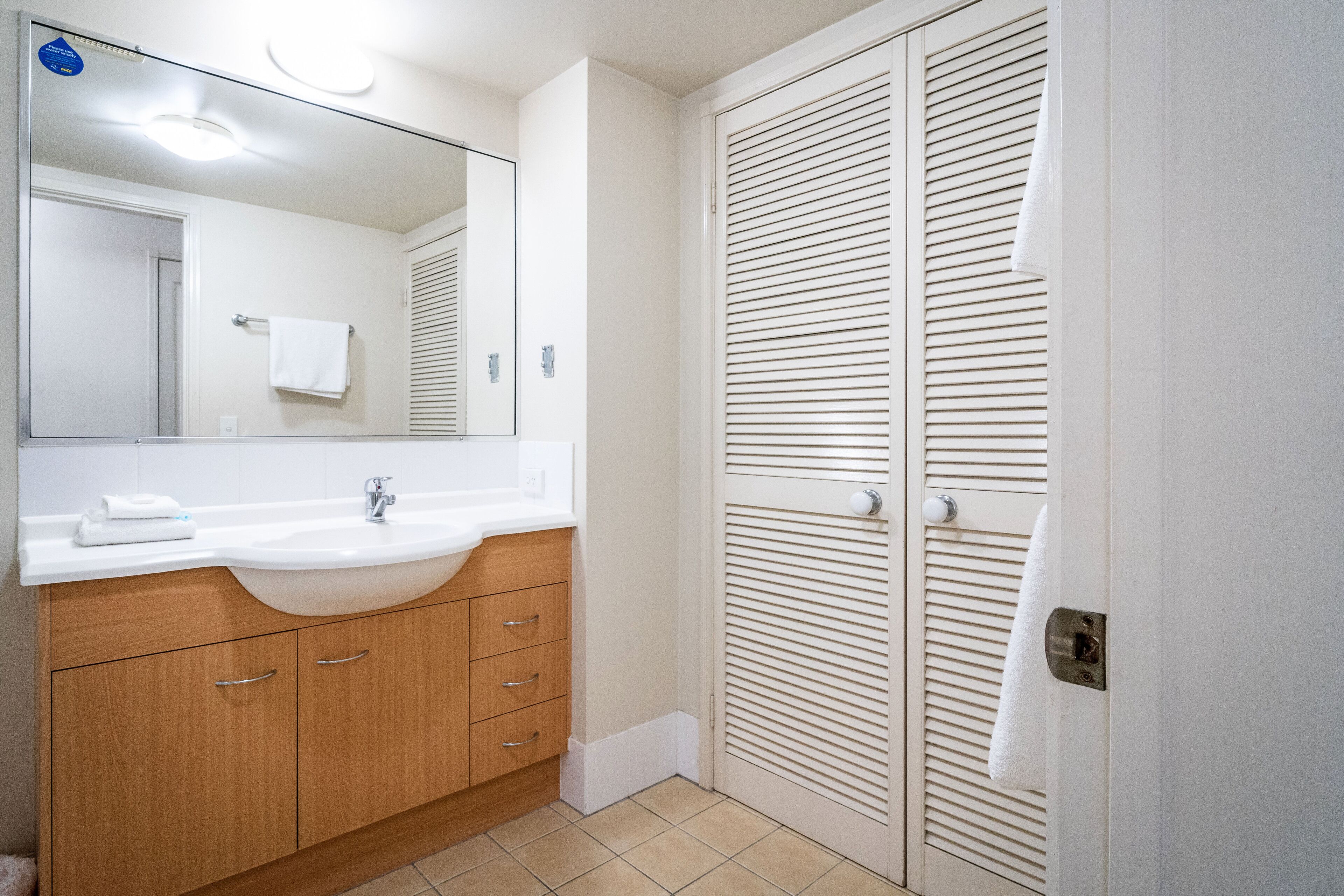 A bathroom with a sink, mirror, wooden cabinets, and a white towel hanging on the door.