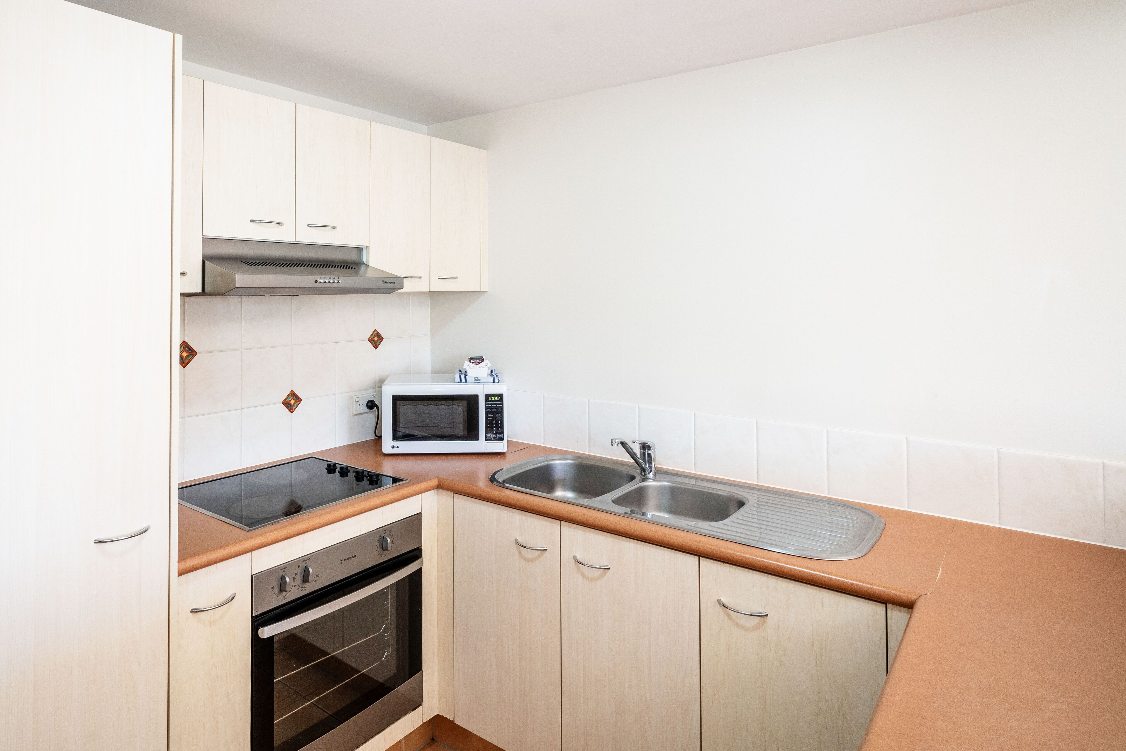 A compact kitchen with white cabinets, a microwave, a stove, and a sink.