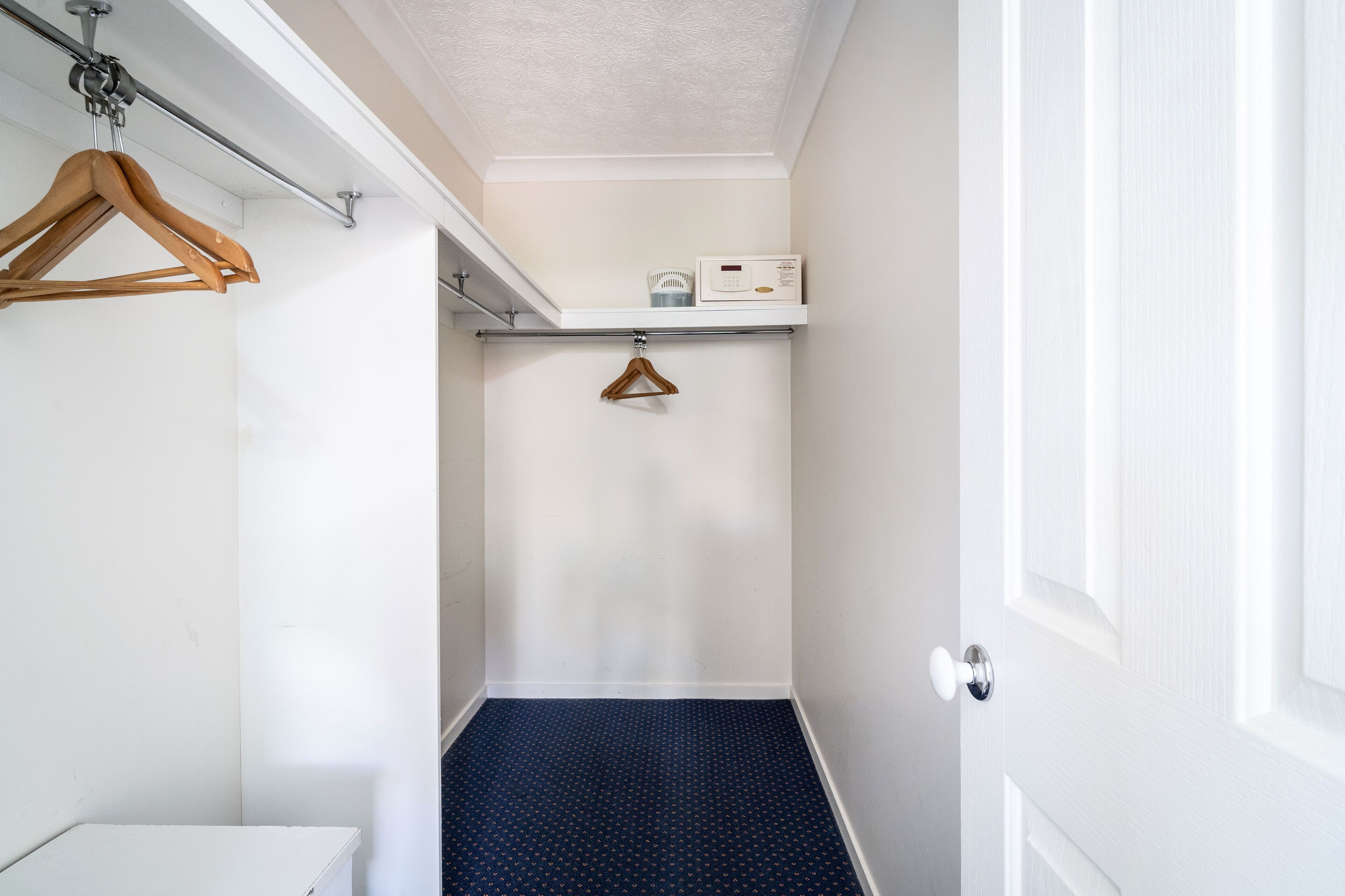 Un pasillo estrecho con una puerta blanca a la derecha, un perchero de madera a la izquierda y un estante con una radio sobre la puerta.