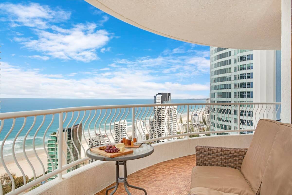 A balcony with a view of the beach and ocean, a table with snacks, and a wicker sofa.