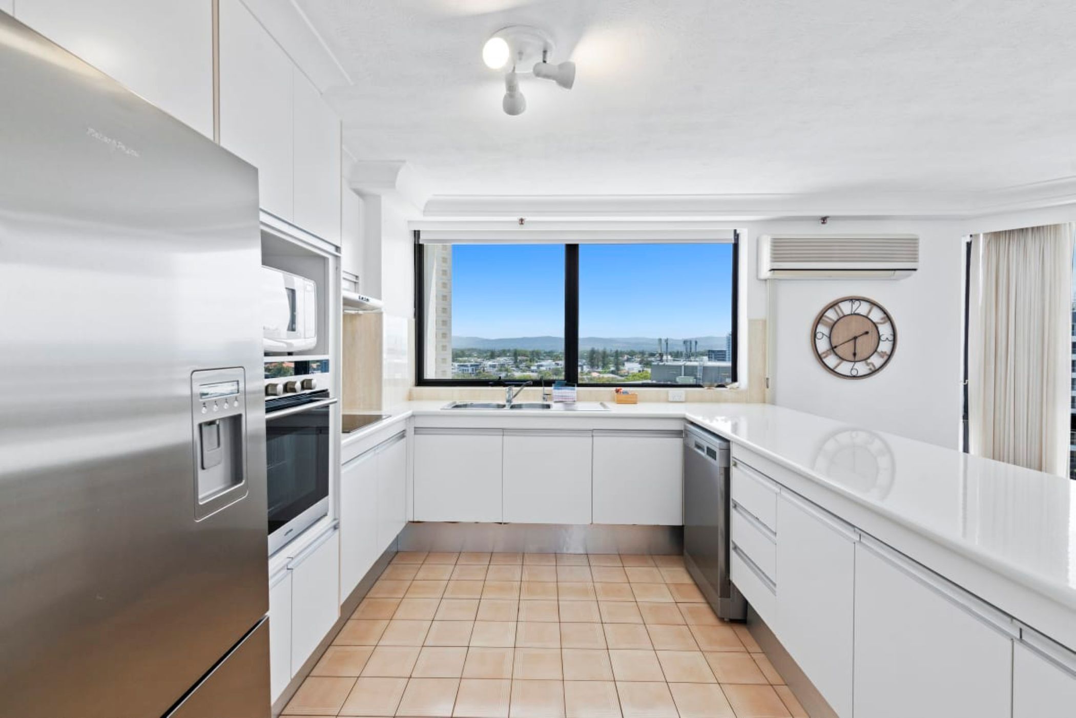 A modern kitchen with white cabinetry, a stainless steel refrigerator, a built-in oven, a microwave, and a window with a city view.