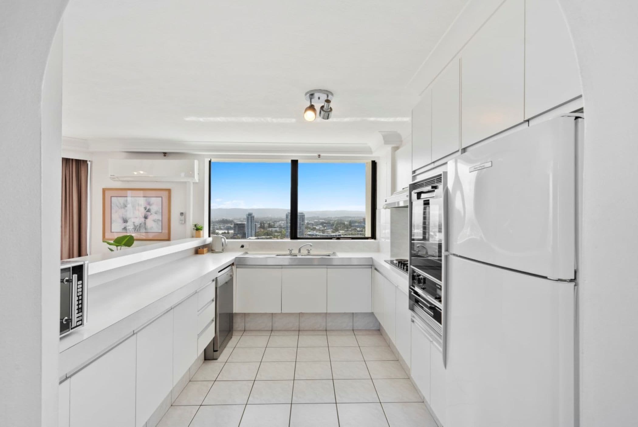 Una cocina moderna con armarios blancos, horno empotrado y un amplio ventanal con vistas a la ciudad.