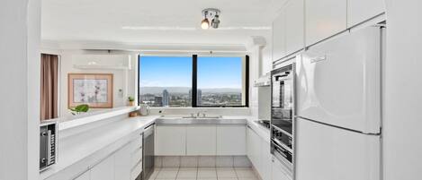 Una cocina moderna con armarios blancos, horno empotrado y un amplio ventanal con vistas a la ciudad.